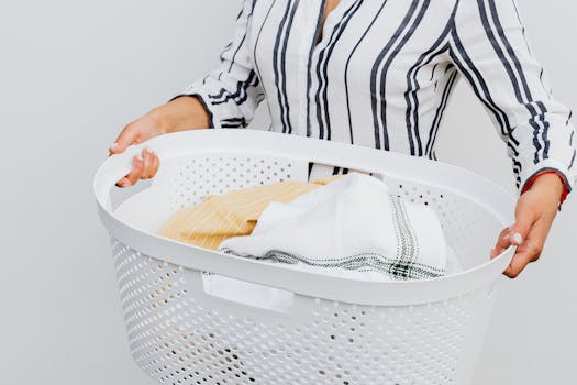 A close-up of a woman holding a white laundry basket filled with fresh, clean clothes.